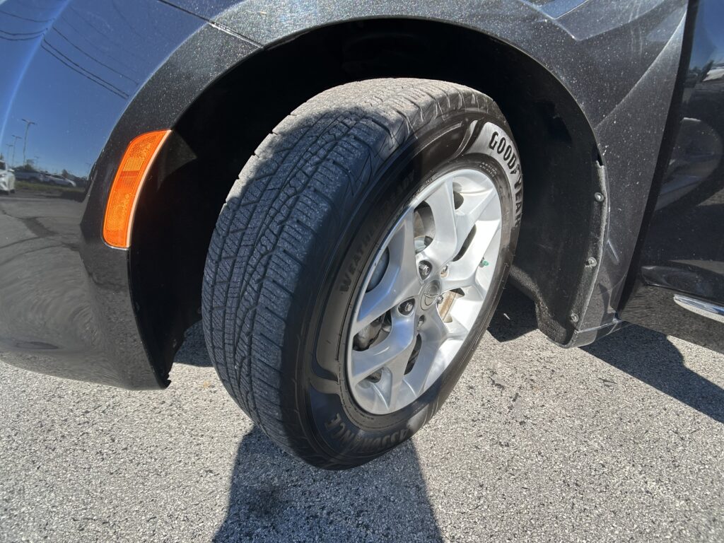 Close-up of a car tire and silver alloy wheel, with a black fender and orange side marker on a dark vehicle.
