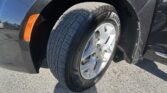 Close-up of a car tire and silver alloy wheel, with a black fender and orange side marker on a dark vehicle.