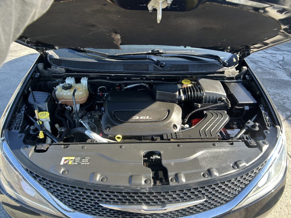 Open car hood showing engine bay with 3.6L engine cover and front grille visible.