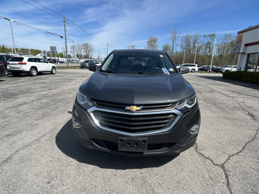 Front view of a dark gray Chevrolet SUV in a sunny dealership lot with other cars in the background.