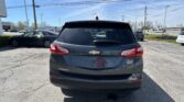 Rear view of a gray Chevrolet Equinox parked in a lot with other cars and a blue sky overhead.