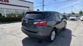 Dark gray SUV in a dealership lot with a white sales building and many cars under a blue sky