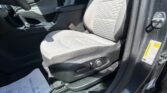 Front interior of a car: gray patterned front seat, center console, gear shifter, and seat belt buckle by the door frame with a yellow caution sticker nearby.