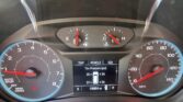 Dashboard view from the driver's seat showing speedometer and tachometer with red needles, plus fuel and engine temperature gauges and a central digital display