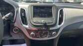 Driver's-eye view of a car dashboard with an infotainment screen, climate controls, and gear shifter; a sunny parking lot visible through the windshield.