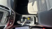 Interior of a car showing the front center console with controls, gear shifter, cup holder, and light-gray patterned seats; papers on the floor mat area.