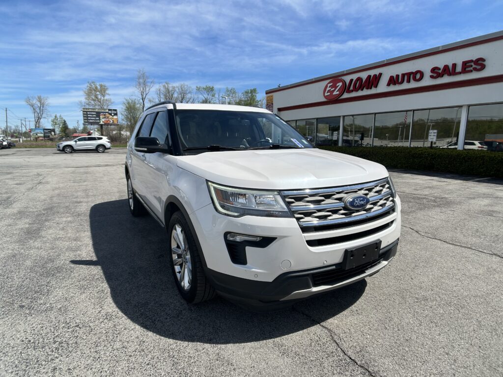 White Ford SUV in the foreground of a car lot, with an EZ Loan Auto Sales storefront in the background under a blue sky.