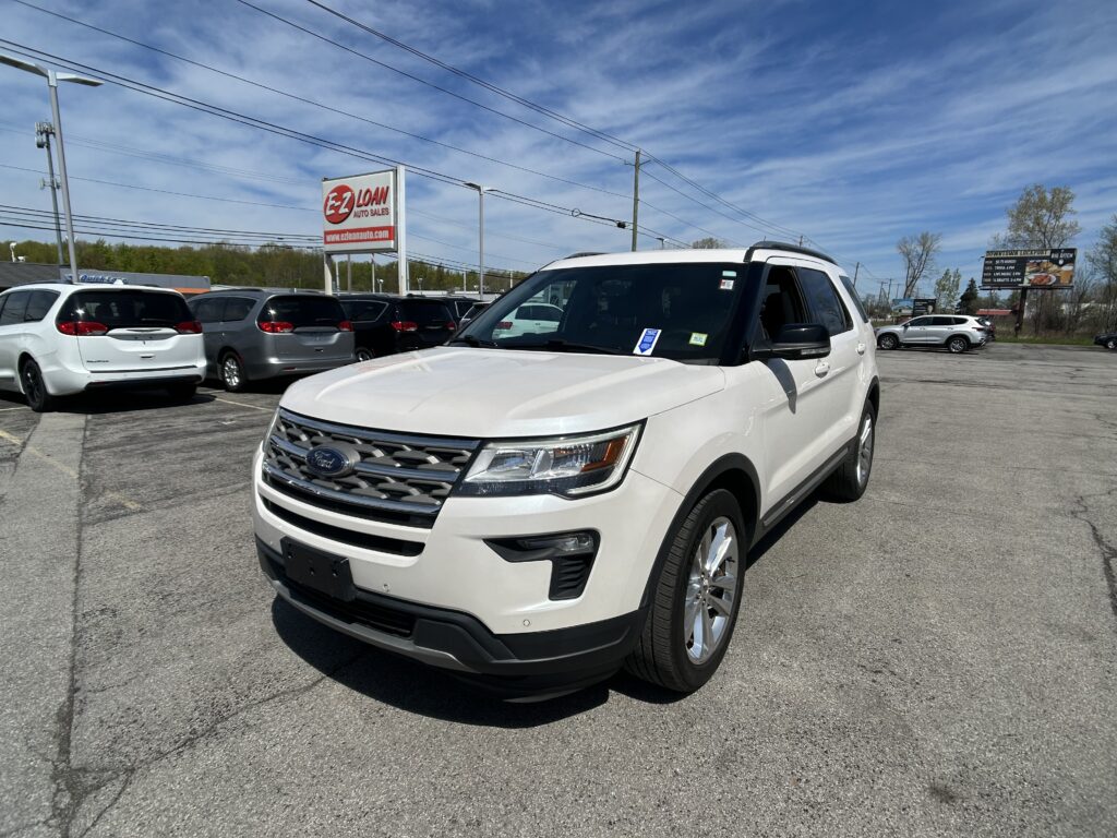 White Ford SUV in the foreground of a car dealership lot with a blue sky and EZ Loan Auto Sales sign in the background.