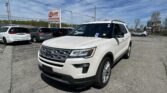 White Ford SUV in the foreground of a car dealership lot with a blue sky and EZ Loan Auto Sales sign in the background.