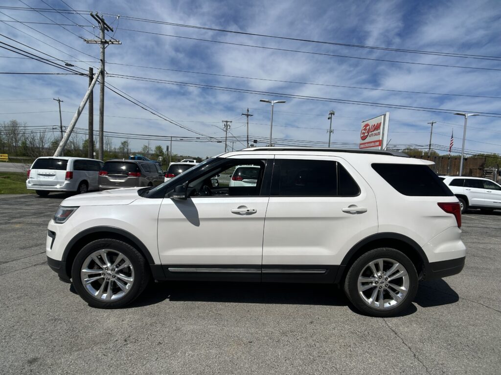 White SUV in a dealership parking lot with power lines overhead and an EZ LOAN Auto Sales sign in the background.