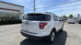 White Ford SUV in a dealership lot with rows of cars and a building in the background under a blue sky.