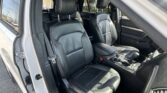 Inside a black leather SUV with front seats and center console visible, sunlit from open door at a car dealership lot behind.