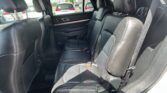 Rear row of black leather seats in an SUV, with headrests and seat belts visible, window to parking lot outside