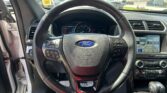 Interior front view of a Ford showing the steering wheel centered, with the speedometer and infotainment screen visible to the right.