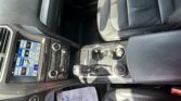 Interior of a car focusing on the center console: touchscreen climate control, gear shifter, cup holders, and leather seats visible in daytime light.