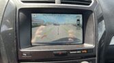 In-car display showing rearview camera view with parking guidelines and a warning: 'Please check surroundings for safety'.