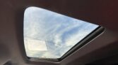 View from inside car showing an open sunroof with blue sky and white clouds above.