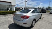 Silver sedan in the foreground at a car dealership lot, with a Toyota dealership building and many parked cars visible in the background under a blue sky.