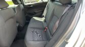 Interior of a car's back seat showing three seats with seat belts and headrests, parked in a lot outside