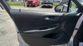Interior of a car door panel viewed from the driver’s seat, with a showroom and parked trucks visible outside the window.