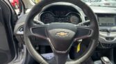 Driver's-seat view of a Chevrolet steering wheel, dashboard instruments, and center console in a parking lot; other cars visible outside through the windshield.