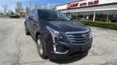 Dark blue Cadillac SUV in the foreground parking lot, in front of an EZ LOAN Auto Sales storefront on a sunny day.