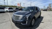 Close-up of a blue Cadillac SUV in a car dealership lot with white minivans in the background and an EZ Loan sign nearby.