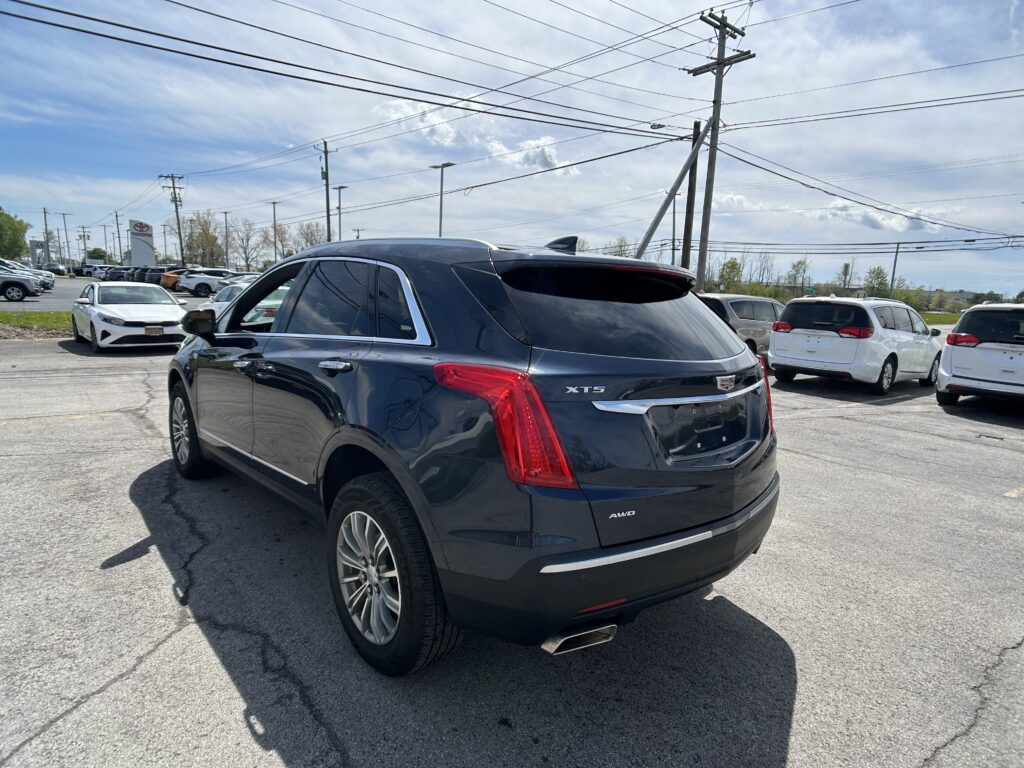Dark blue Cadillac XT5 SUV in a parking lot, foreground, with power lines and other vehicles in the background at a dealership.
