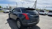 Dark blue Cadillac XT5 SUV in a parking lot, foreground, with power lines and other vehicles in the background at a dealership.