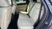 Rear passenger seat area of a beige leather SUV with two rows of seats visible and seat belts fastened in place.