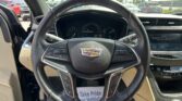 Driver's-seat view of a Cadillac interior, featuring the steering wheel with emblem, instrument cluster, and center touchscreen; parked in a lot.