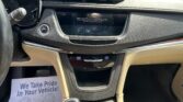 Inside a car: center touchscreen shows a warning message, gear shifter labeled P R N D, and a flyer on the left reading 'We Take Pride In Your Vehicle!'