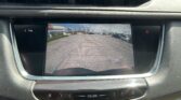 Infotainment screen showing the car's rearview camera feed with parking guideline lines in a parking lot.