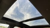 Interior view from a car showing raindrops on the panoramic sunroof and a blue sky outside.