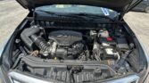 Car engine bay with hood up, showing the air intake, battery, and coolant reservoir in a dark engine compartment.