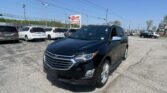 Black Chevrolet SUV in the foreground at a car dealership, with white minivans in a row behind it and an EZ LOAN Auto Sales sign in the distance against a clear blue sky.