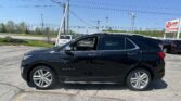 Black Chevrolet Equinox SUV parked in a dealership lot with power lines and utility poles overhead; sign for EZLOAN Auto Sales visible in the background.