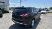 Rear view of a black Chevrolet SUV in a sunny dealership lot with other cars and an American flag in the background