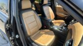 Interior of a black car with tan leather front seats and a center console visible from the open rear door.