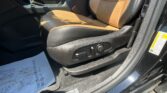 Interior of a car showing tan leather front seats, a center console with the gear shifter, and black plastic trim; sunlight highlights the seat and door frame with a warning sticker nearby.