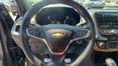 Steering wheel close-up inside a Chevrolet, with dashboard gauges and center infotainment screen in view; outside parking lot seen through windshield
