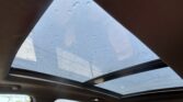 View from inside a car of a panoramic sunroof with raindrops on the glass and blue sky beyond (outdoor scene seen through glass).] ,