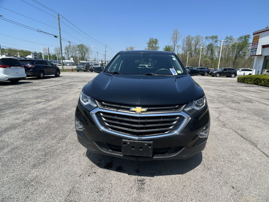 Front view of a black Chevrolet SUV parked in a sunny car dealership lot, with other vehicles around and a building in the background.