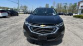Front view of a black Chevrolet SUV parked in a sunny car dealership lot, with other vehicles around and a building in the background.