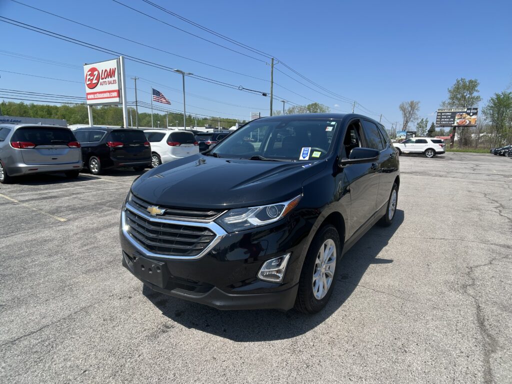 Black Chevrolet SUV in the foreground at a car dealership lot with other vehicles and an EZ LOAN sign in the background.