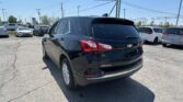 Rear three-quarter view of a black Chevrolet Equinox in a crowded dealership parking lot on a sunny day, with other cars in the background and power lines overhead.