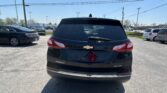 Rear view of a black Chevrolet Equinox parked in a car lot, with other vehicles and overhead power lines in the background.