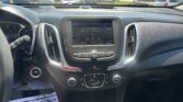 Interior of a car showing the center console with a touchscreen, climate controls, and gear shifter; a 'THANKS FOR COMING IN' sign is visible on the floor mat.