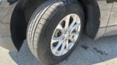 Close-up of a car's front wheel: tire with tread, silver alloy rim with Chevrolet emblem, and dark wheel well behind it.