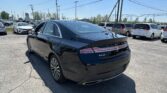 Black Lincoln MKZ in the foreground at a sunny car dealership lot, with white minivans parked behind and a clear blue sky above.